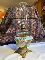 Full view of 19-inch tall ornate oil lantern showing the floral ceramic base, ornate metal foot, and tall clear glass chimney.