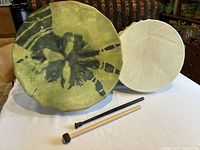 Two vintage First Nation ceremonial drums side by side on table with two wooden drum beaters in front.