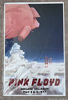 Photo showing the Pink Floyd 11 x 17 concert poster in protective sleeve. Artwork depicts a large floating pig over fog with Golden Gate Bridge and concert details.