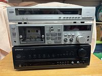Front view of the Hitachi FT-4000 FM stereo tuner, Technics M250 cassette deck loaded with a cassette tape, and Pioneer SX-303R stereo receiver stacked below on a wooden surface.