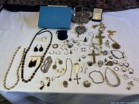 Wide view showing assortment of vintage costume jewelry on white cloth background, including necklaces, rings, earrings, brooches, and pendants arranged flat.