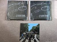 Photo of two new unopened LP album frames with black metal borders and glass fronts alongside the sealed Beatles Abbey Road vinyl album