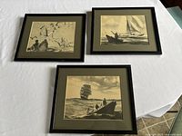 Set of three framed monochrome sketches of marine scenes laid out on a tabletop.