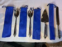 Full view of the four serving utensils with their blue fabric protective cases laid out on a white cloth background.