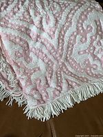 Close-up of the textured white and pink chenille pattern with tassel trim on one edge of the bedspread.