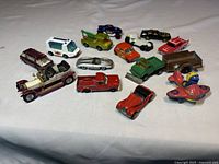 Overview of 13 vintage die cast toy vehicles in various colors and types, arranged on a white fabric surface