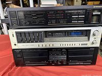 Three stacked vintage stereo components on red cloth: Pioneer amplifier on top, Fisher receiver in the middle, Kenwood cassette deck bottom.