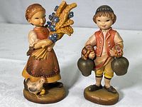 Pair of ANRI Swiss carved wood figurines, girl with flowers and boy with cow bells, standing side by side on a flat surface.