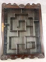Front view of the display shelf with closed hinged glass door showing the Asian motif carved wood frame and compartment design behind the glass.
