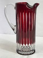 Side view of ruby red cut-to-clear crystal pitcher showing smooth clear handle and vertical fluted design.