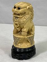 Front and side view of the ivory-colored carved Chinese guardian Foo Dog showing detailed facial features, collar, and paw holding ball.