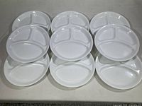 Photo showing all nine Corelle white 3-section divided plates arranged in rows, seen from top.