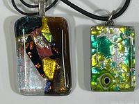 Close-up image showing both fused glass pendants side by side on black cords with visible colorful abstract designs in glass.