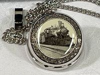 Front view of pocket watch showing locomotive illustration under glass dome and surrounding rhinestone border with attached chain.