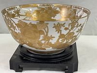 Side view of white porcelain bowl showing gold floral design on the exterior and the solid wood stand beneath it.
