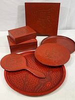 Group photo showing all items in the lot including platters, plates, mirror, and lidded boxes in red lacquer with carved designs.