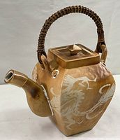 Full view of large decorative pottery teapot showing square body, spout, lid, and rattan handle