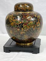 Front view of large brass cloisonné covered jar on black wood stand showing full floral pattern.