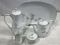 Full coffee and tea set with platter showing all five pieces including coffee pot, tea pot, creamer, sugar bowl, and platter, all white fine china with rose pattern and silver trim.