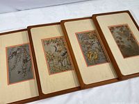 Four framed engraved metal wall art pieces with beige linen matting and wood frames, laid out side by side