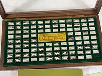 Wooden display case open showing 99 sterling silver mini ingots arranged in green velvet insert with central identifying plaque