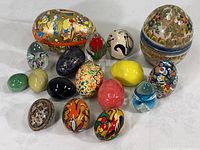 Collection of 15 colorful decorative collectible eggs of various materials including stone, glass, paper, and ceramic, arranged on white surface.