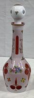 Front view of the pink cranberry cased glass decanter showing the floral hand painted decorations and gold accented design on the neck and body.