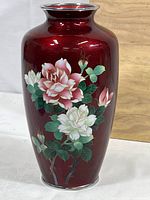 Front view of brass cloisonné vase with oxblood red finish and floral design, showing the pink and white flowers with green leaves.
