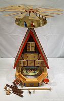 Full view of the assembled vintage German Christmas pyramid showing the large rotating fan blades on top, triangular central structure with folk art painted details, and candle holders at the base. Loose pieces and figurines are displayed in front.