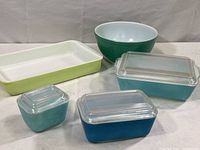 Group photo showing all vintage Pyrex ovenware items: a green serving bowl, lime green casserole, two light blue casseroles with lids, and a blue covered dish.
