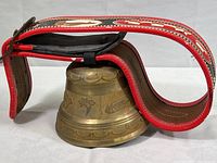 Full side view of brass cowbell with the leather collar strap folded over it, showing decorative pattern.