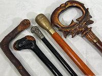 Five vintage walking canes arranged side-by-side on white cloth background, showing top handles.