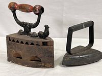 Side view of both irons side by side, showing wood handle and rooster on larger iron, simpler design on smaller iron.