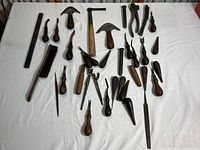 Overview of all woodworking and hand tools arranged on white cloth, includes two wooden hammers, multiple carving tools, brushes, and pliers.