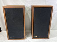 Front view of two rectangular wooden speakers with black fabric grilles and small Epicure logo on one grille.