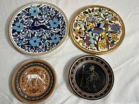 Four different decorative plates arranged on a flat surface showing their painted designs.