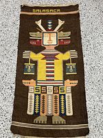 Full view of handwoven Southwestern tapestry showing central figurative motif with animal heads and vibrant geometric patterning on dark brown background.