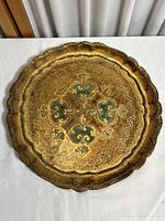 Front view of round wooden tray with gold finish and green floral design in center.