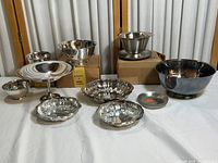 Full collection of silver plated and stainless steel bowls and serving dishes on white cloth