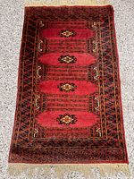 Full view of the Persian geometric wool rug with red base and black and orange geometric patterns and fringed edges.