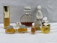 Full front view of all 8 perfume bottles showing variation in size, shapes, and colors with liquids inside bottles and a white ceramic figurine bottle