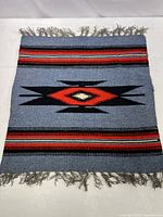 Top-down full view of the small woven rug showing the geometric pattern, color scheme, and tassel fringes on both short ends