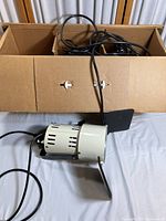 Single Smith Victor Q 60 video lighting unit shown with black adjustable barn doors and attached power cord, placed in front of cardboard box that contains additional lighting units and cords.