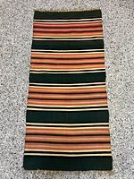 Top full view of small wool runner rug showing its striped multicolor pattern and overall condition.