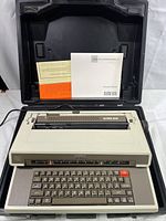Front view of the Royal Alpha 2001 electric typewriter inside its carrying case, showing the keyboard, paper feed area, and instruction manuals.