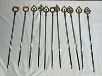 Full set of 10 vintage brass and metal skewers with ornate finials, laid out horizontally on white background.