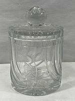 Front view of the clear crystal lidded jar showing engraved floral and leaf pattern on the jar body with fluted vertical lines.