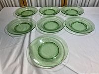 Seven vintage green glass shallow bowls arranged on a white surface, displaying the full set from above.
