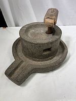 Stone grain grinder showing top view with stone grinding area and wooden handle inserted vertically.