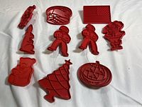 Full set of red plastic vintage Tupperware cookie cutters arranged on white surface, showing variety of holiday themed shapes such as Christmas tree, flag, gingerbread men, and more.